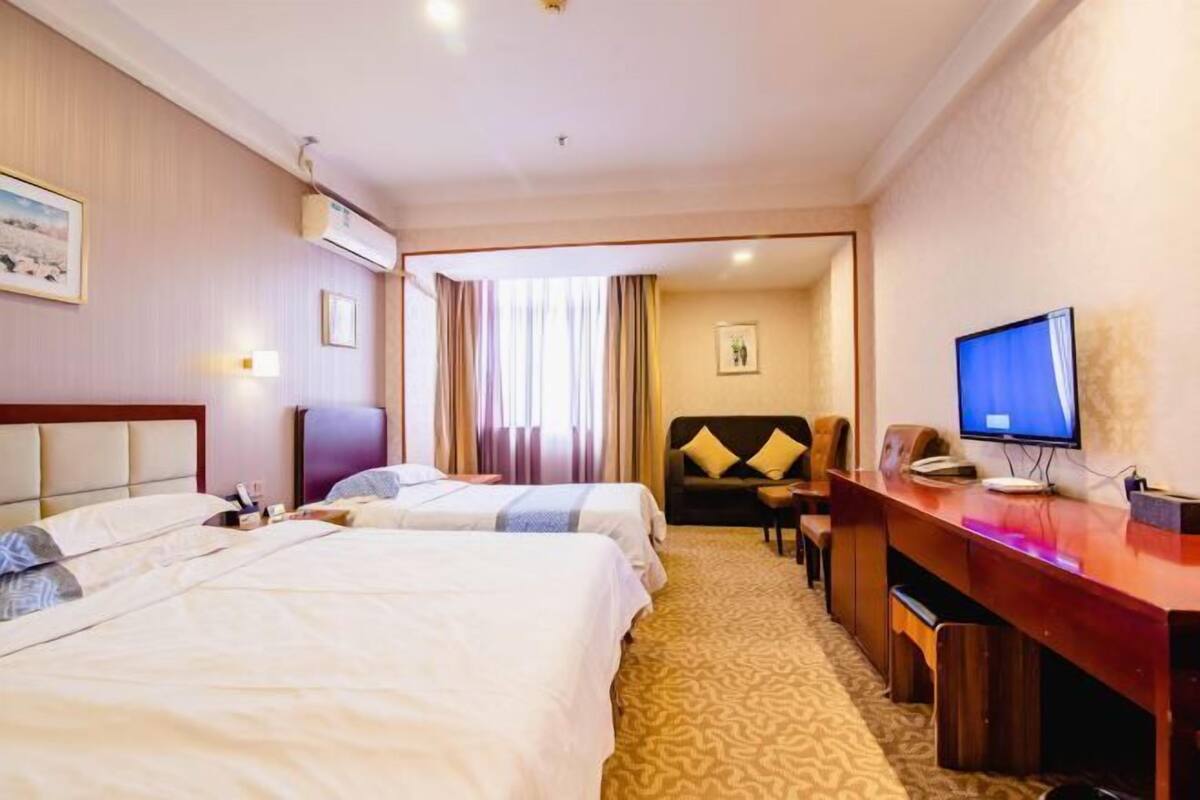 A hotel room with two beds, a desk, a television, and a view of the hallway.