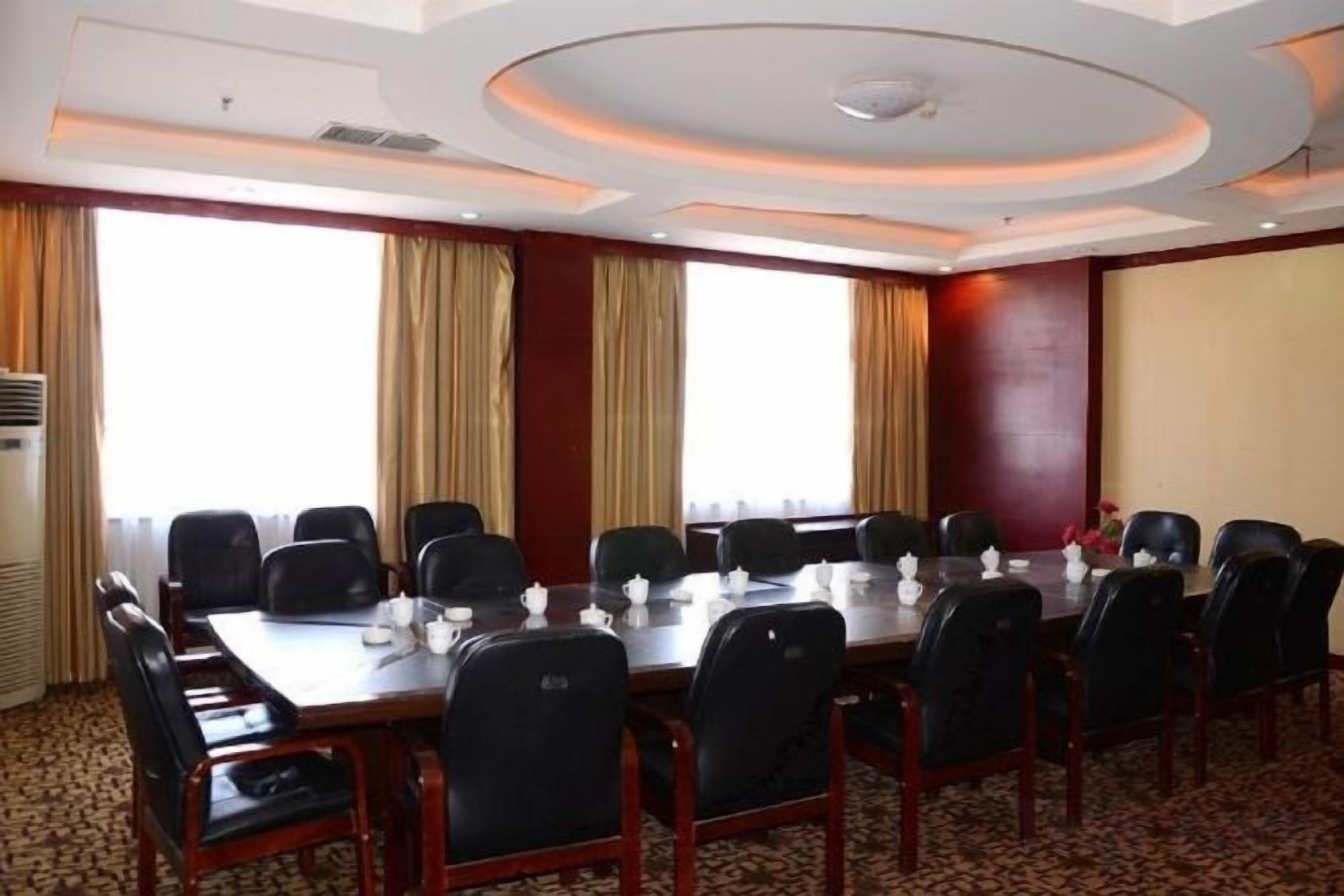 Uma sala de conferências com uma mesa comprida, cadeiras e uma grande janela com cortinas.