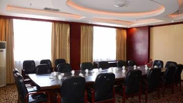 Uma sala de conferências com uma mesa comprida, cadeiras e uma grande janela com cortinas.