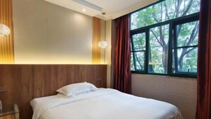 Cama bem arrumada em quarto de hotel com uma janela grande e vista para árvores.