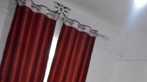 A bed with white and red bedding, a gold headboard, and red curtains with a white trim. - Stay.Plus Mwanzo Apartment Eldoret (Eldoret)