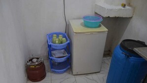 A small kitchenette with a refrigerator, a blue plastic basket, a blue barrel, and a brown gas cylinder. - Stay.Plus Mwanzo Apartment Eldoret (Eldoret)
