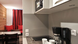 A compact kitchen with a coffee maker, a small stove, and a dining area with a table and chairs.
