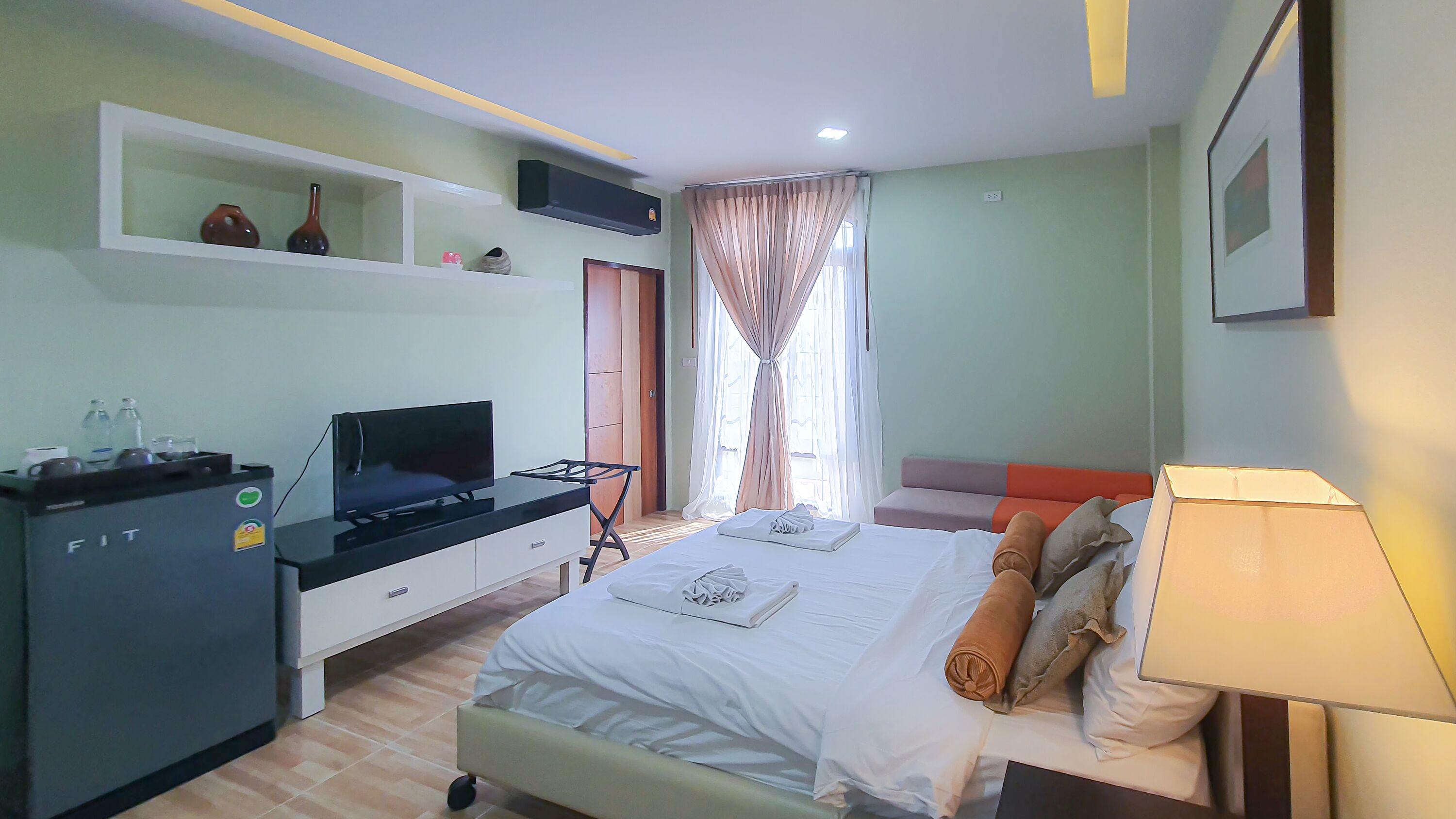 Habitación de hotel con cama, escritorio con televisor, estante con adornos y ventana con cortinas.