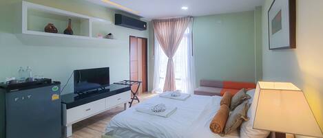 Habitación de hotel con cama, escritorio con televisor, estante con adornos y ventana con cortinas.