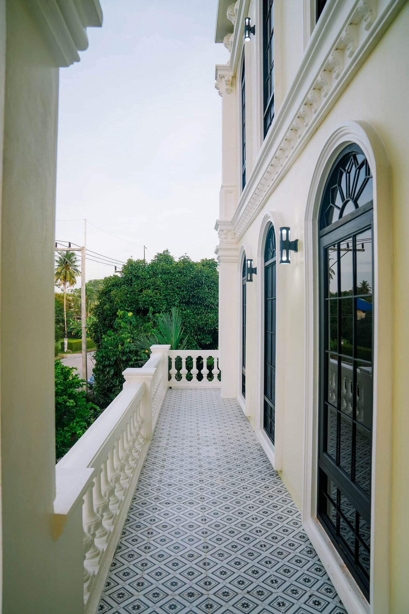Varanda com piso estampado, balaústres brancos e janelas grandes com molduras pretas.