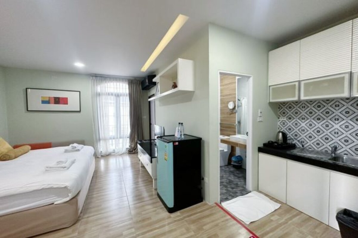 Habitación de hotel compacta con cama, kitchenette, un refrigerador pequeño y baño a la vista a través de una puerta abierta.