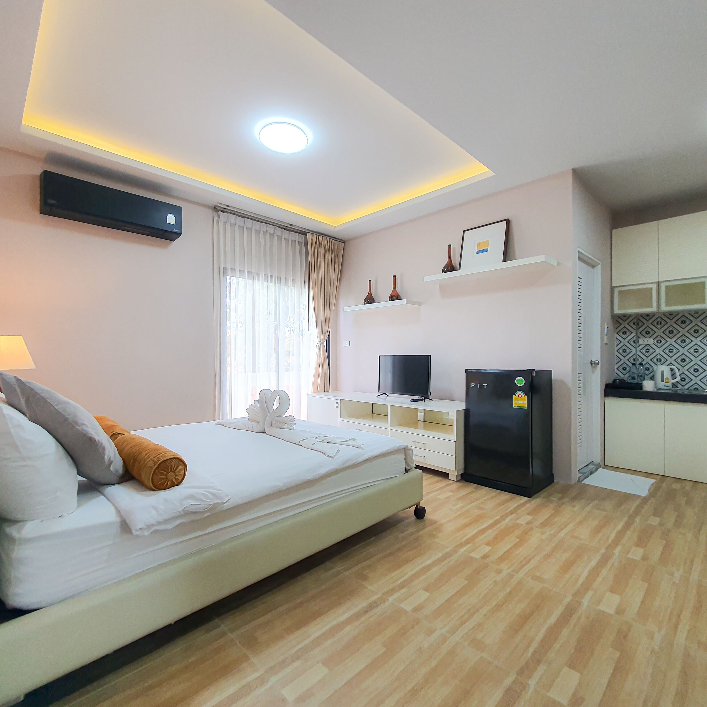 A hotel room with a bed, a TV, a refrigerator, and a kitchen area.