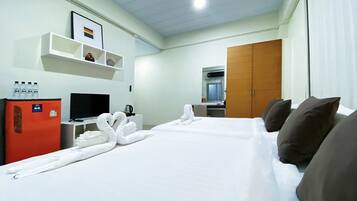 Quarto de hotel com cama, televisão, frigorífico, prateleira com artigos de higiene e roupeiro.