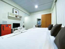 Quarto de hotel com cama, televisão, frigorífico, prateleira com artigos de higiene e roupeiro.
