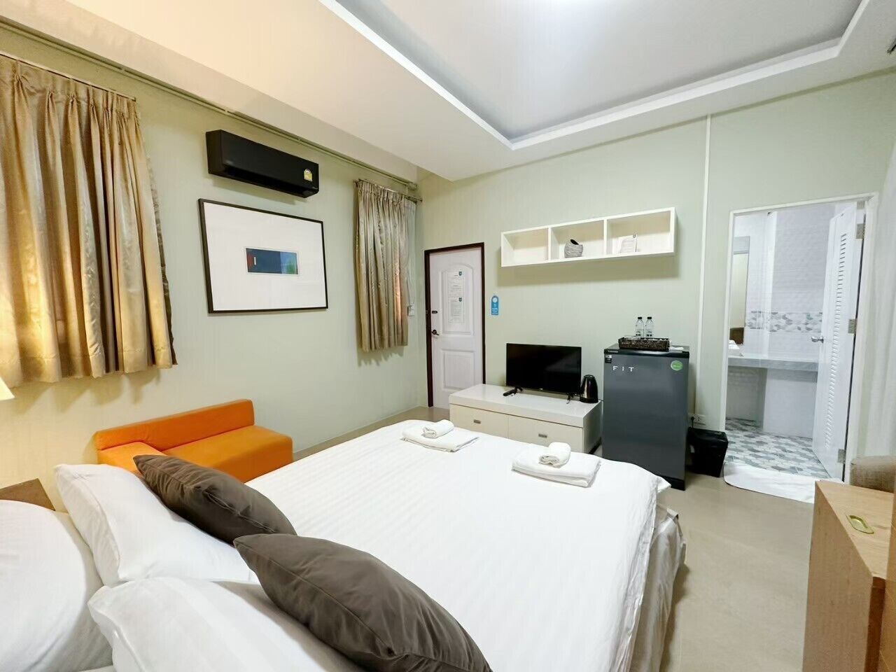 A hotel room with a bed, a desk, a television, a minibar, and a bathroom.