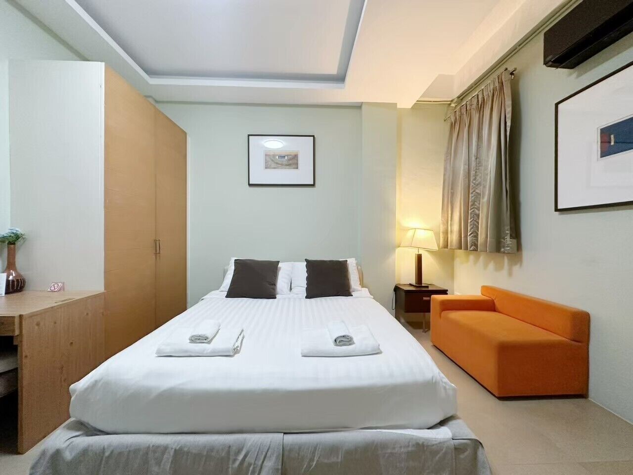Una habitación de hotel con una cama, un escritorio, una silla, un sofá, una lámpara y un cuadro en la pared.