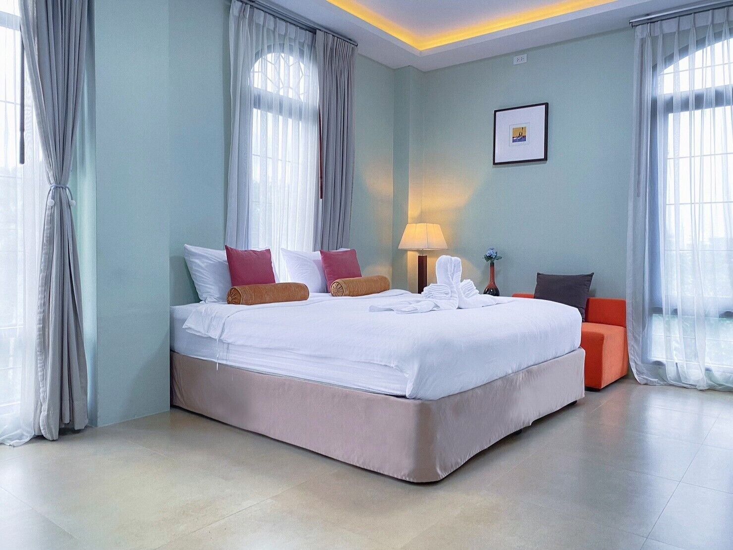 Quarto de hotel com uma cama grande, uma mesa de cabeceira com abajur e uma cadeira.