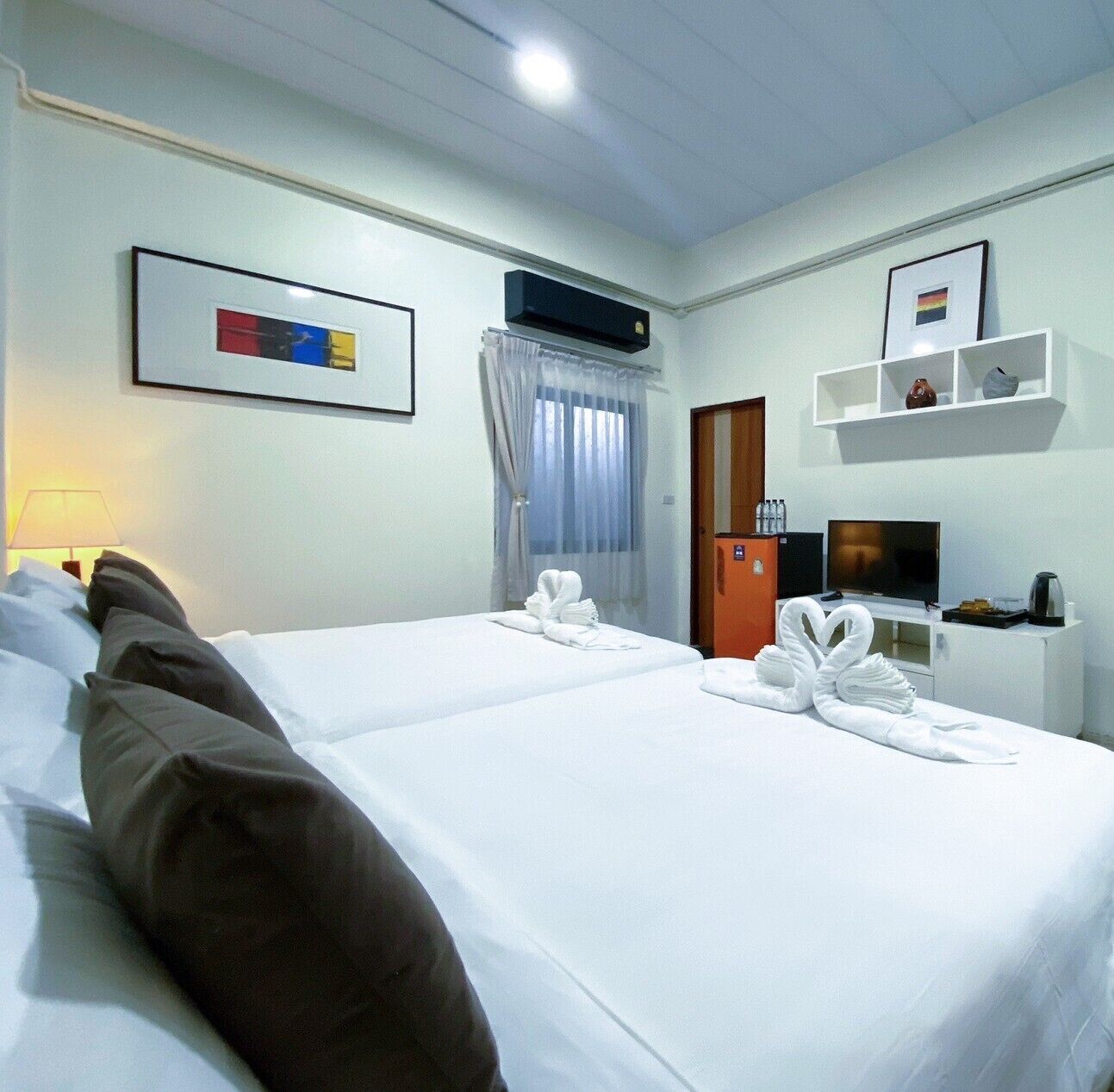 A hotel room with two beds, a TV, a minibar, and a bathroom door.