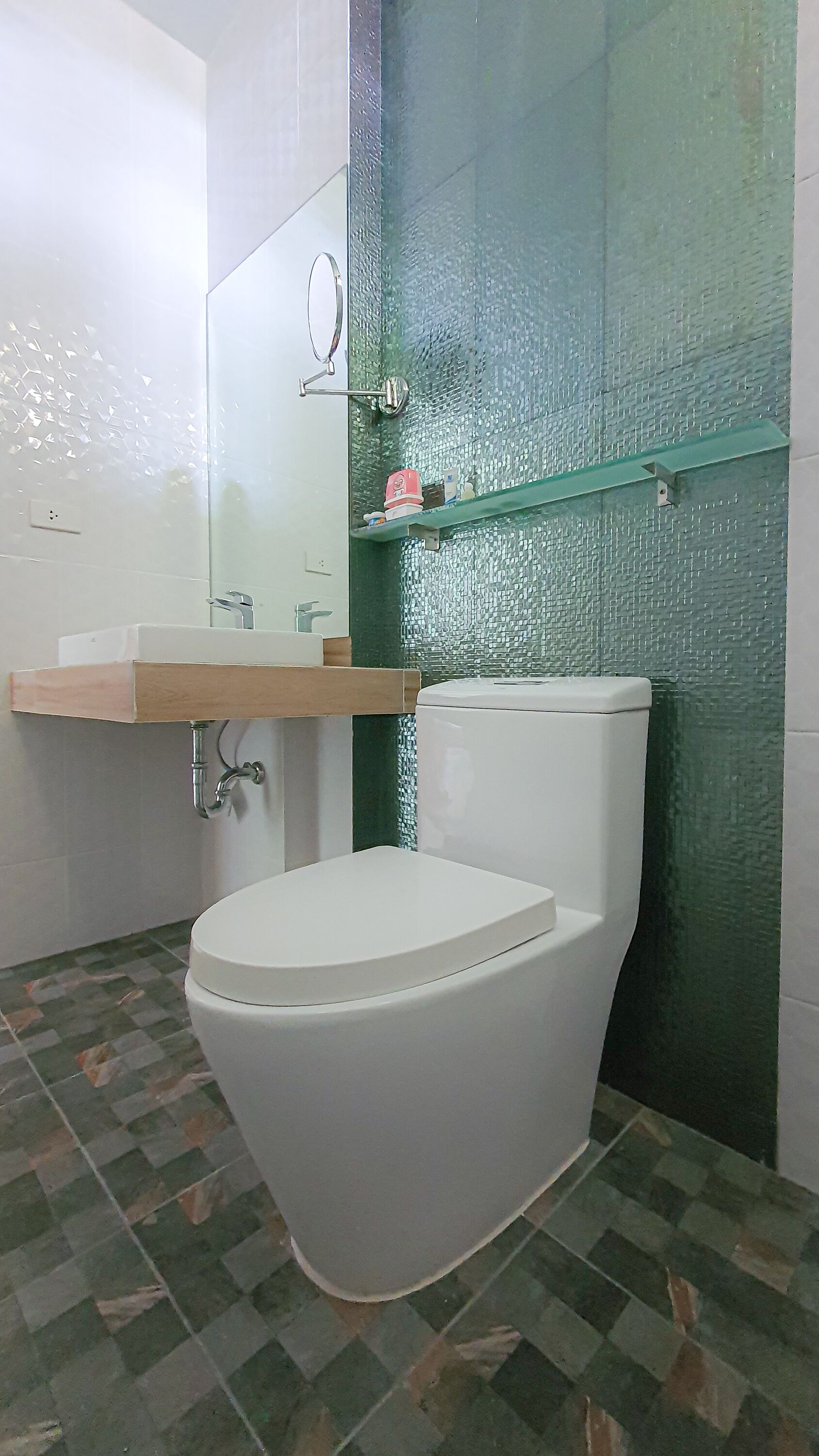 A bathroom with a white toilet, a glass shelf, and a green tiled wall.