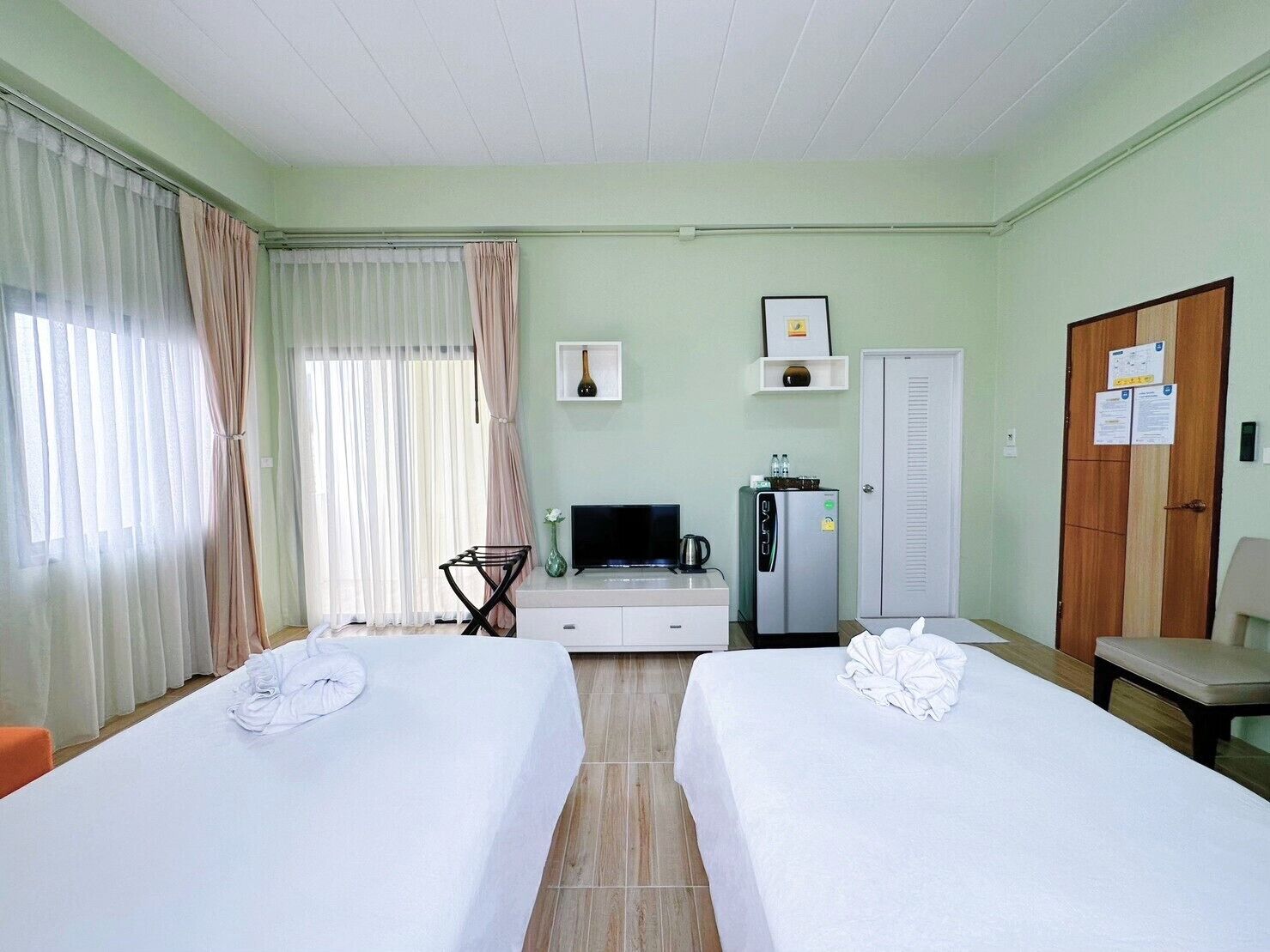 A hotel room with two beds, a television, a refrigerator, a desk, and a wardrobe.