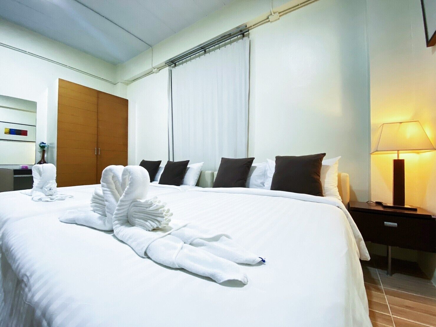 Ein Hotelzimmer mit einem ordentlich bezogenen Bett, einer Nachttischlampe und einem Holzschrank.