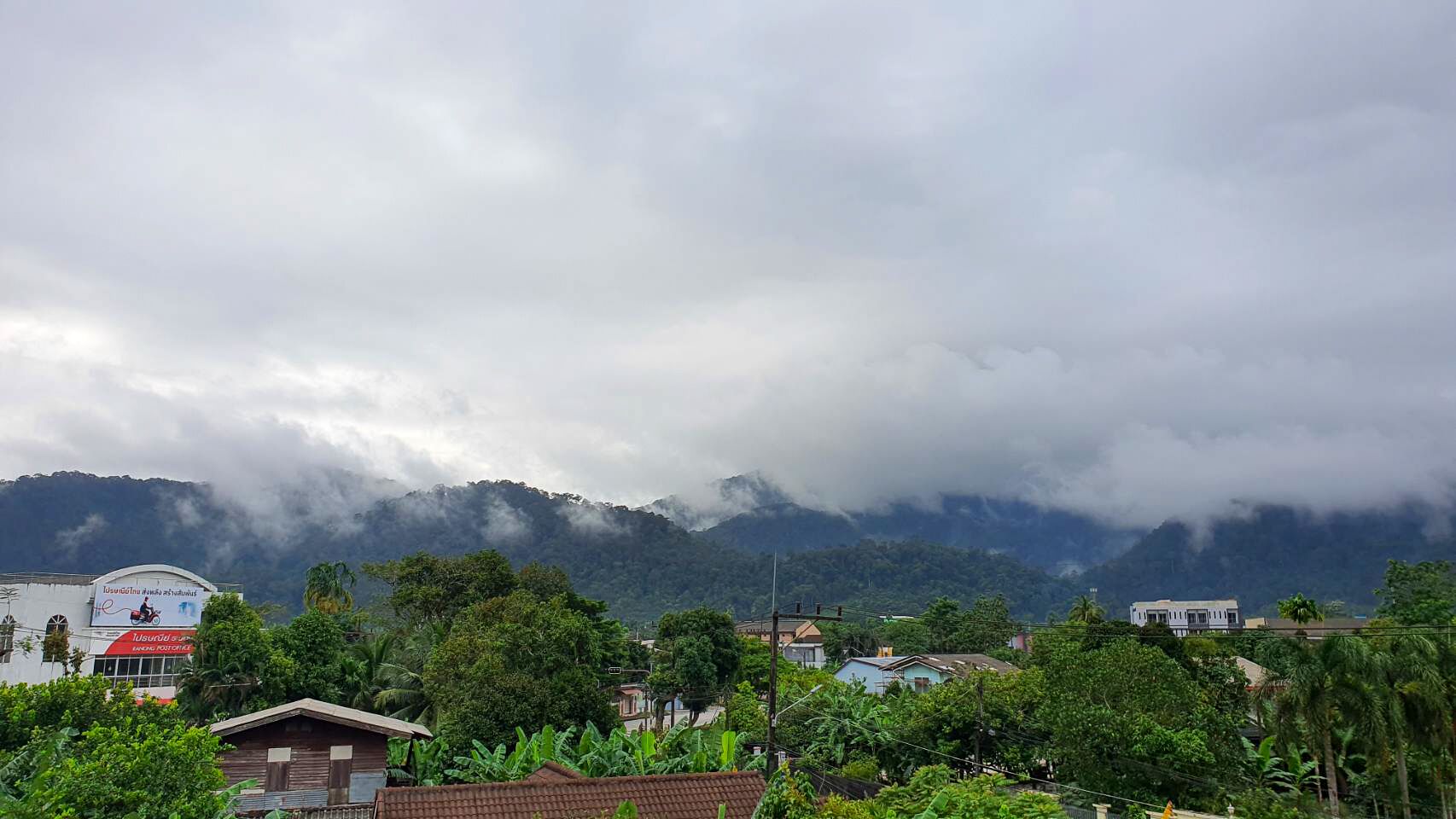 Un paisaje montañoso con nubes, un edificio de techo rojo y vegetación en primer plano.