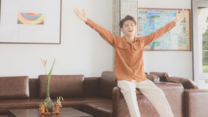 A person sitting on a brown leather couch in a well-lit room with a large window, a framed artwork on the wall, and a small table with a vase and decorative items. - Daddy Dream Hotel and Residence (Ranong)