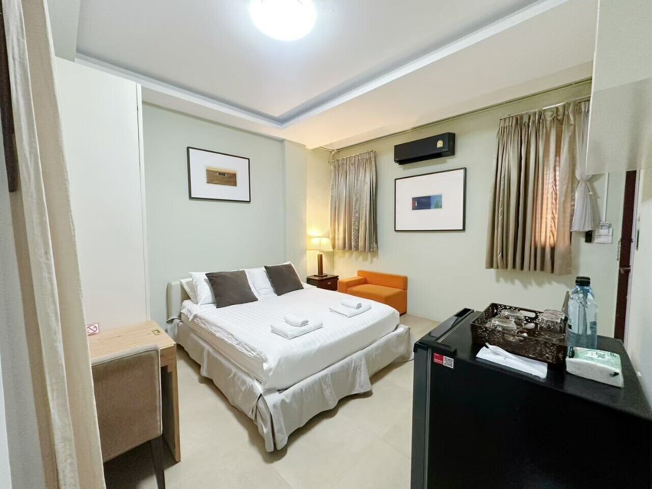 A hotel room with a bed, a desk, a chair, a nightstand, and a lamp.