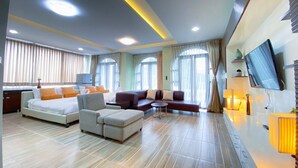 A hotel room with a large bed, a sofa, a small table, a TV, and a window with curtains. - Daddy Dream Hotel and Residence (Ranong)