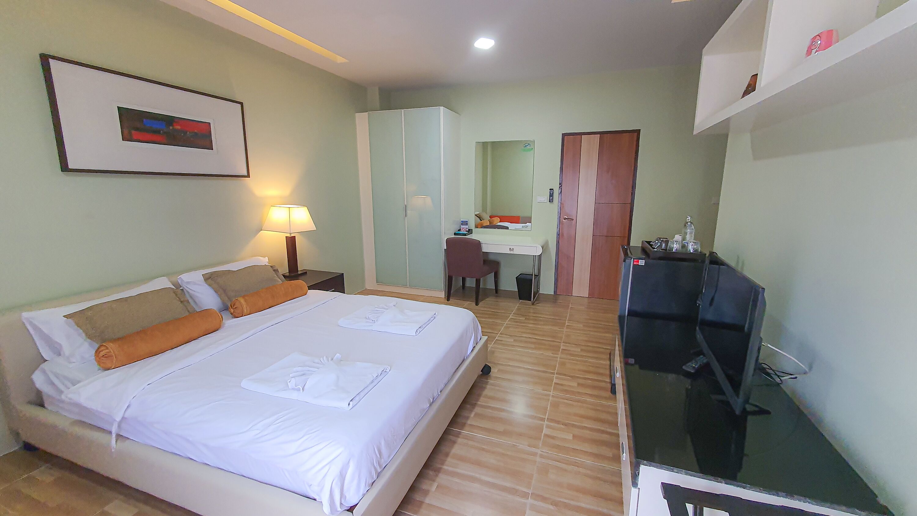 Una habitación de hotel con cama, escritorio, silla, espejo y televisión.