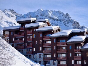Ein mehrstöckiges Hotel mit Balkonen und einem verschneiten Berg im Hintergrund.