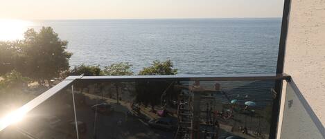 A balcony with a glass railing overlooking a beach and the sea.