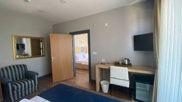 A hotel room with a bed, a desk, a chair, a TV, a mirror, and a window with curtains.