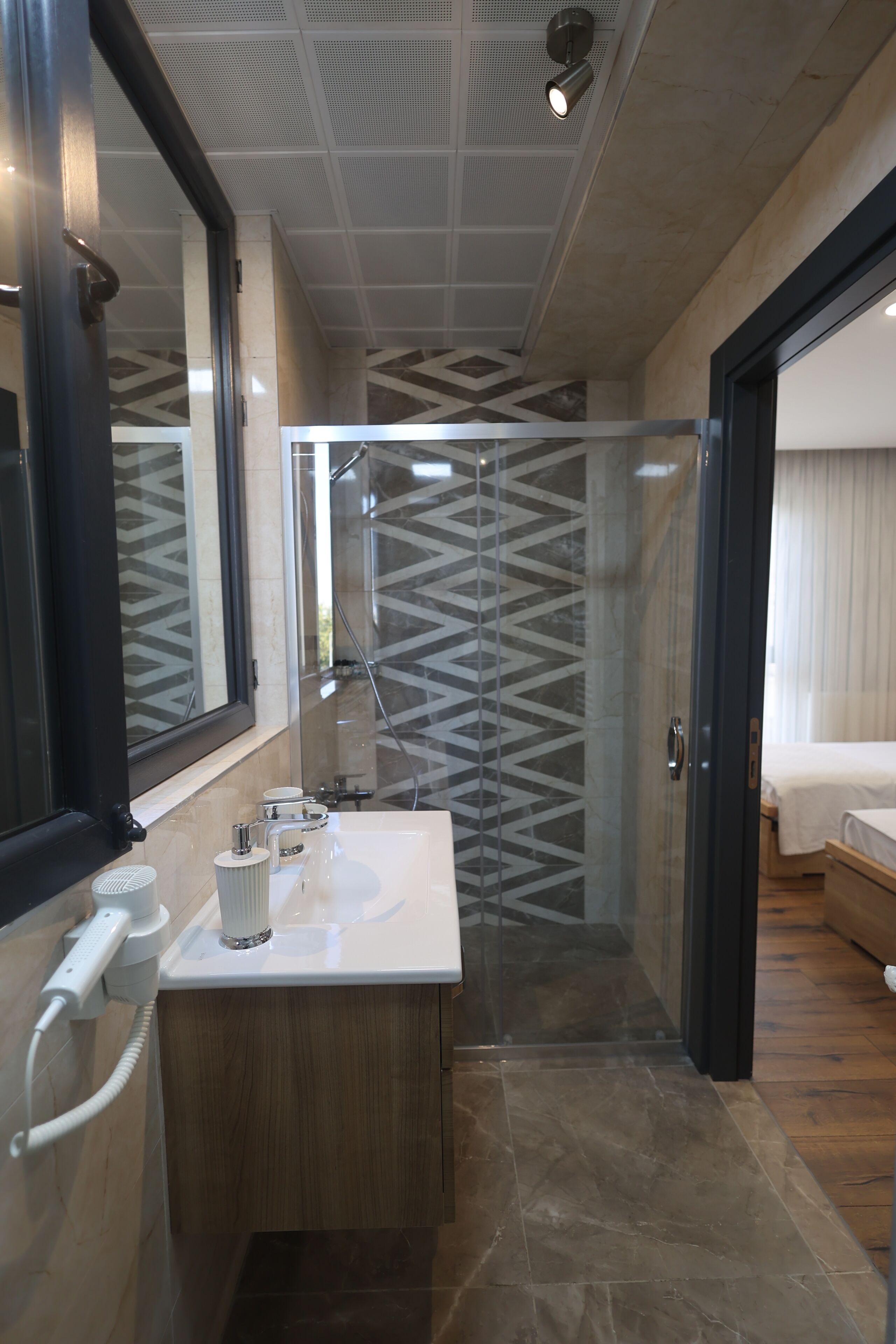 A modern bathroom with a glass shower enclosure, a wooden vanity, and a large mirror.