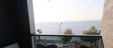 A balcony with a view of the sea, a chair, and parked cars.
