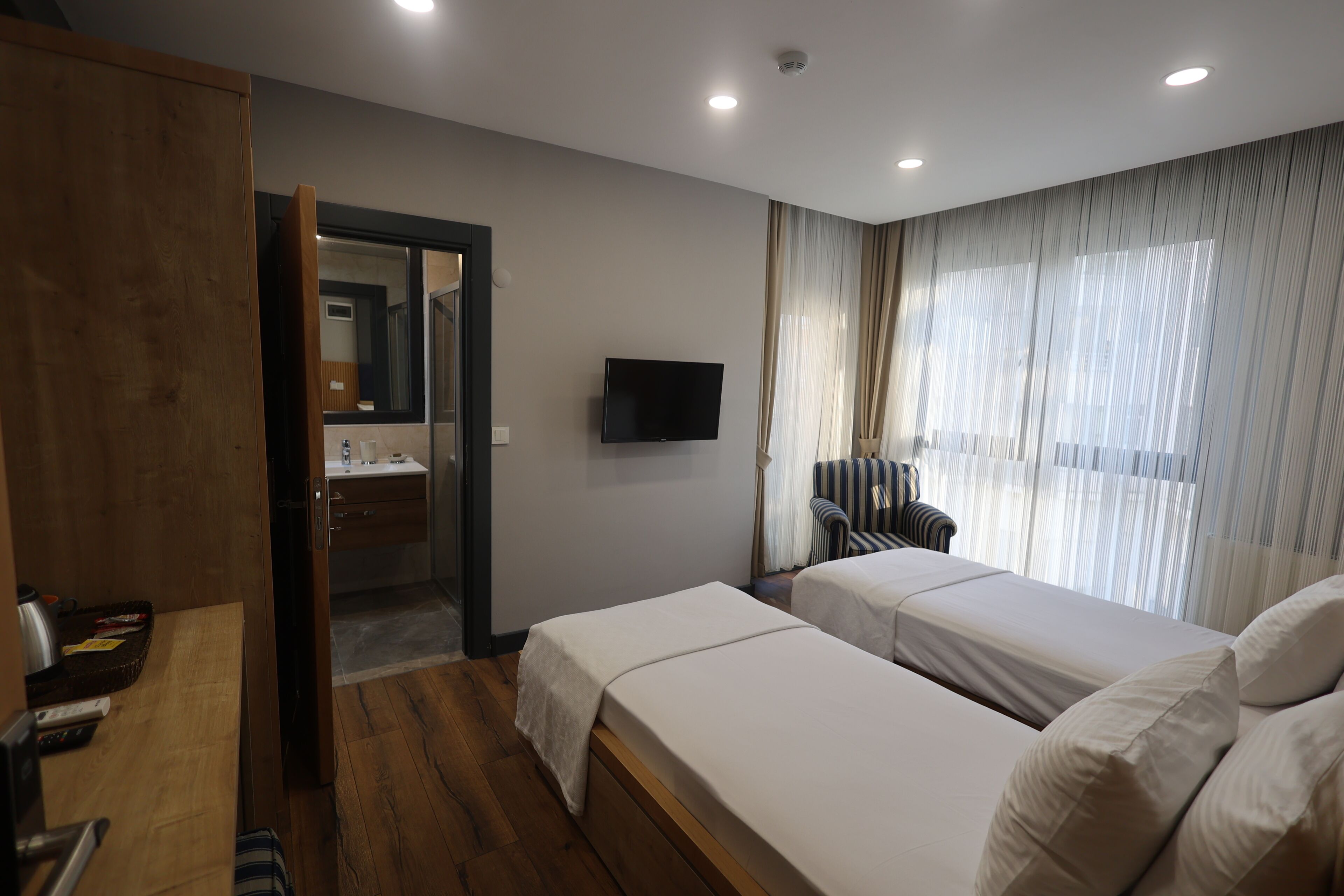 A hotel room with two beds, a TV, a wooden wardrobe, a bathroom, and a window with curtains.