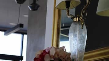 Un candelabro con múltiples lámparas, un espejo con marco dorado y un florero con flores sobre una repisa de chimenea.