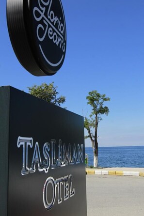 A sign for Tasliman Hotel with a clear view of the sea in the background. - Tasliman Otel (Cinarcik)