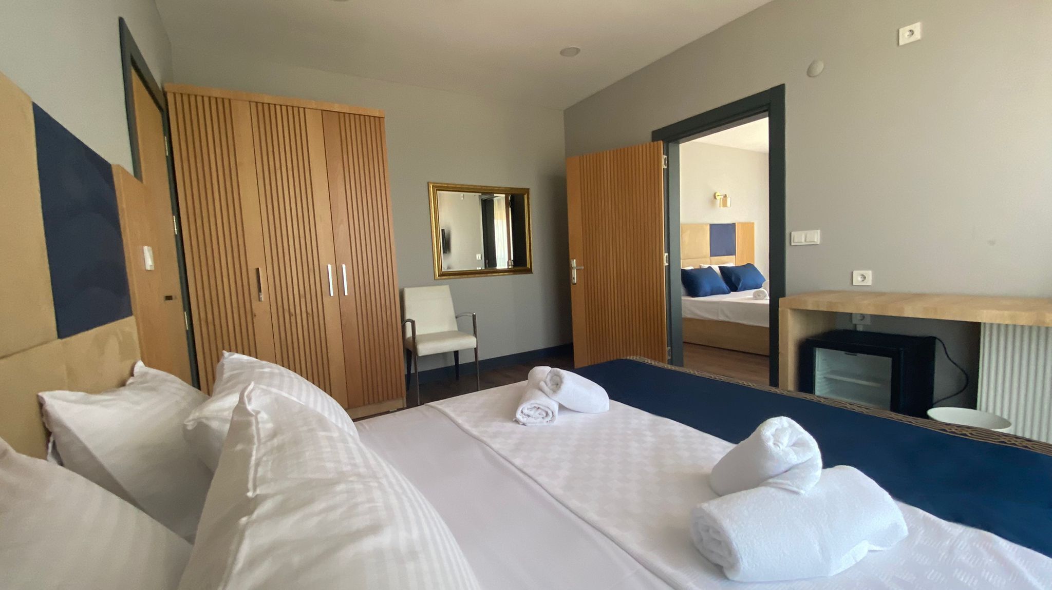 Habitación de hotel con una cama grande, un armario de madera, un espejo, un escritorio y vista a la habitación contigua.