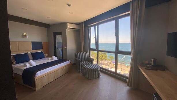 Un dormitorio con cama, una silla, un escritorio y un amplio ventanal con vistas al mar.