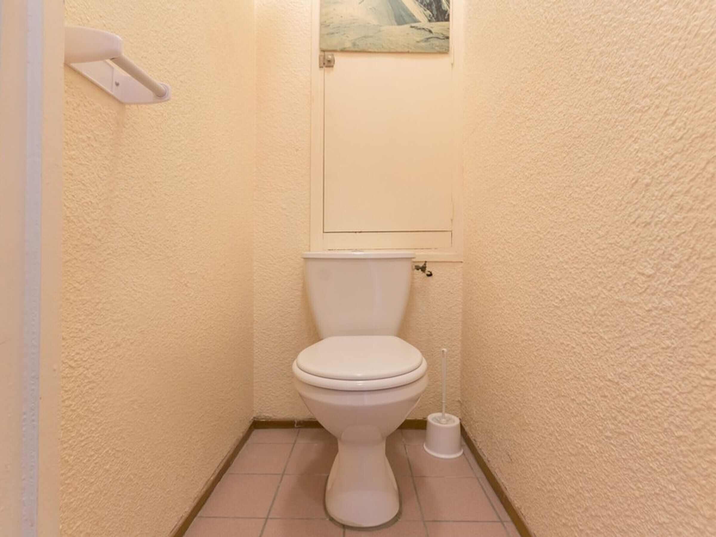 A small, compact bathroom with a toilet, a toilet paper holder, and a small trash bin.