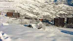 Un paysage montagneux enneigé avec plusieurs bâtiments, dont un hôtel à étages et une station de ski en arrière-plan.