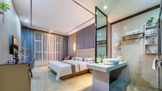 A modern hotel room with a bed, a desk, a large mirror, a bathroom with a sink and towel rack. - Xinjia Fashion Hotel (Guangzhou Shigang East Village Store) (Guangzhou)