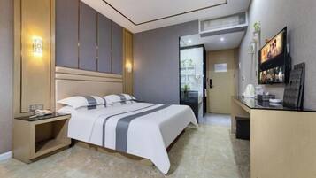 A modern hotel room with a bed, bedside table, and a desk with a flat-screen TV.