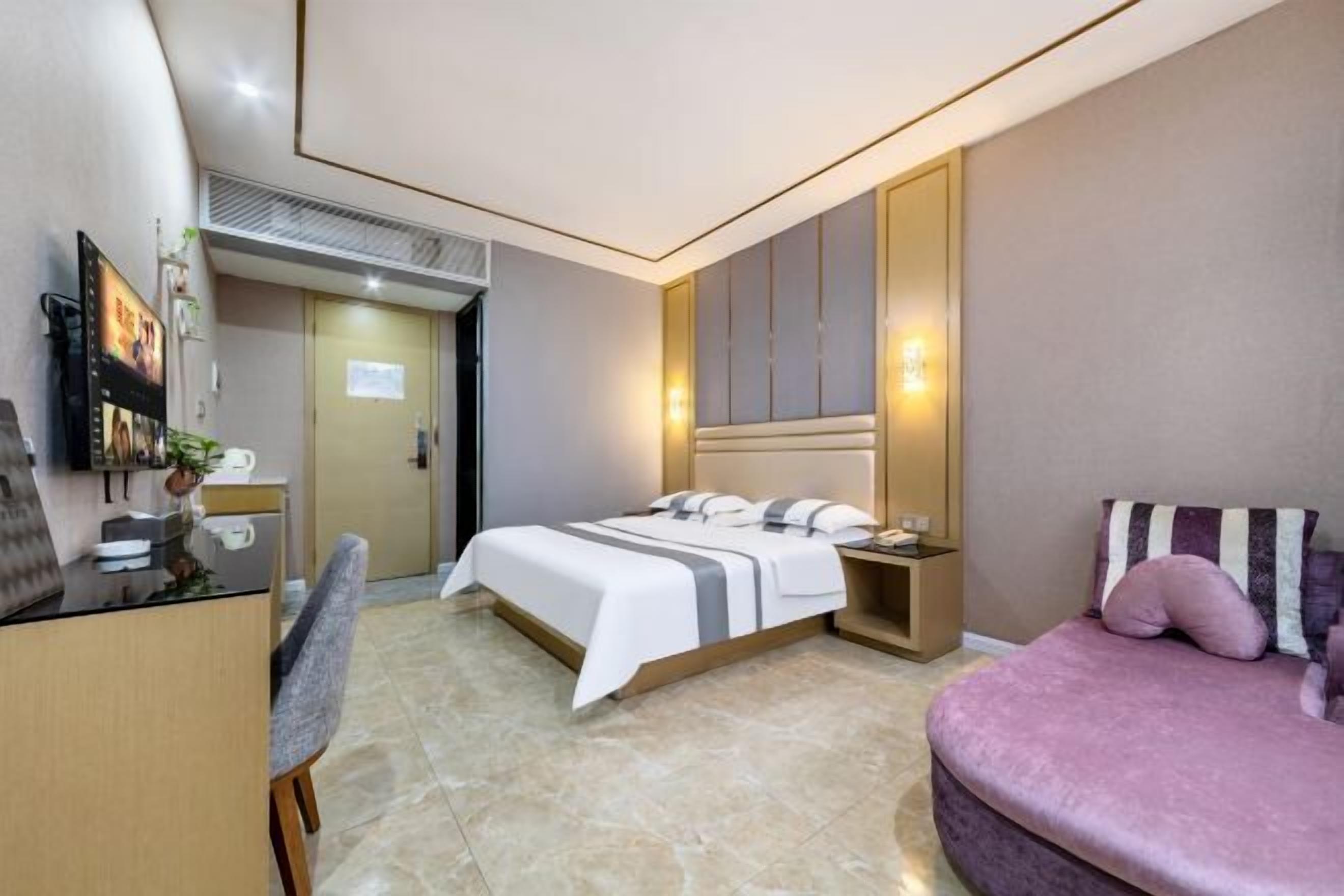 A modern hotel room with a bed, a desk, a chair, a TV, and a sofa.