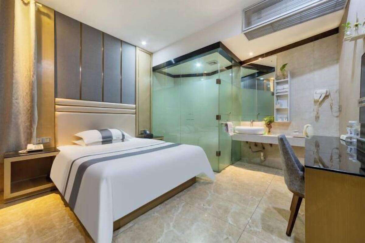 Een moderne hotelkamer met een groot bed, een douche met glazen wanden, een kaptafel met spiegel en een klein bureau.