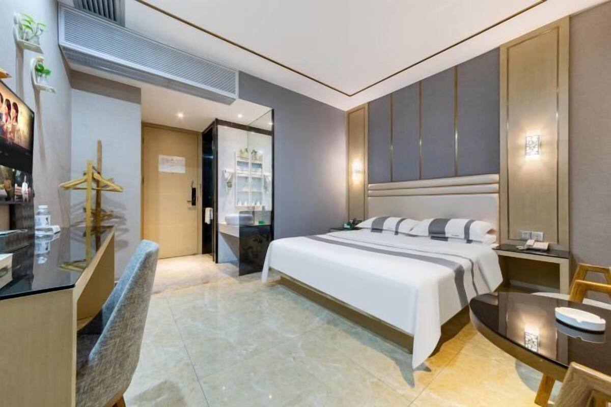 Een moderne hotelkamer met een groot bed, een bureau met stoel, een kaptafel en een badkamer die door een open deur zichtbaar is.