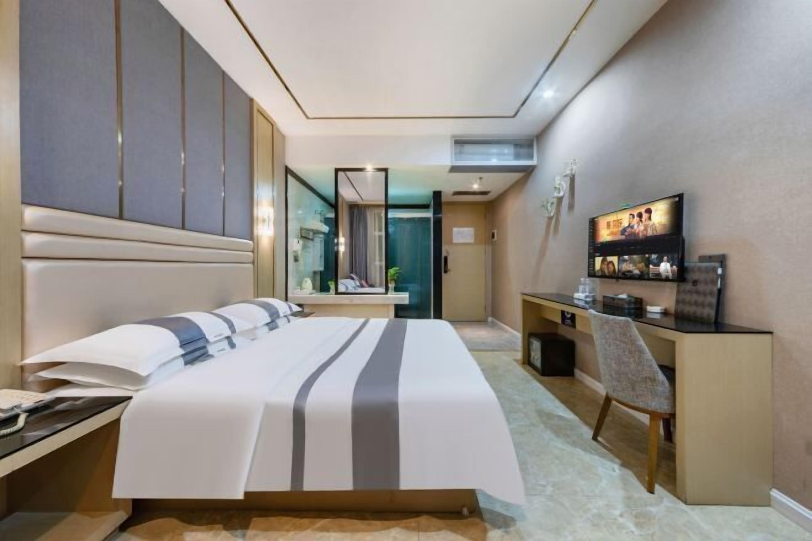 A hotel room with a bed, a desk, a chair, a television, and a mirror.