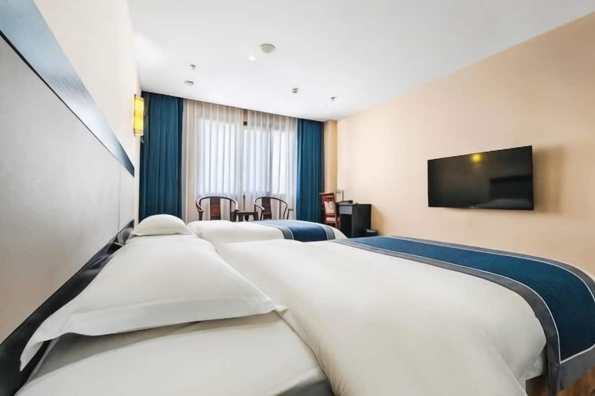 Ein Hotelzimmer mit zwei Betten, einem an der Wand befestigten Fernseher und einem Schreibtisch mit Stuhl.