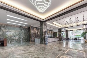 Een ruime lobby met een marmeren vloer, een grote vaas en een moderne kroonluchter.