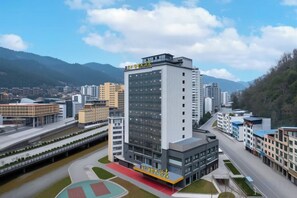 A modern multi-story building with a flat roof, surrounded by a landscaped area with a sports field. - A Fu Er Lian Suo Jiu Dian (Youyang County)
