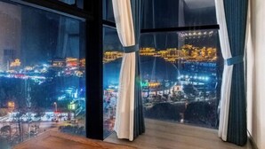 Een kamer met grote ramen en uitzicht op een verlicht stadsbeeld 's nachts.