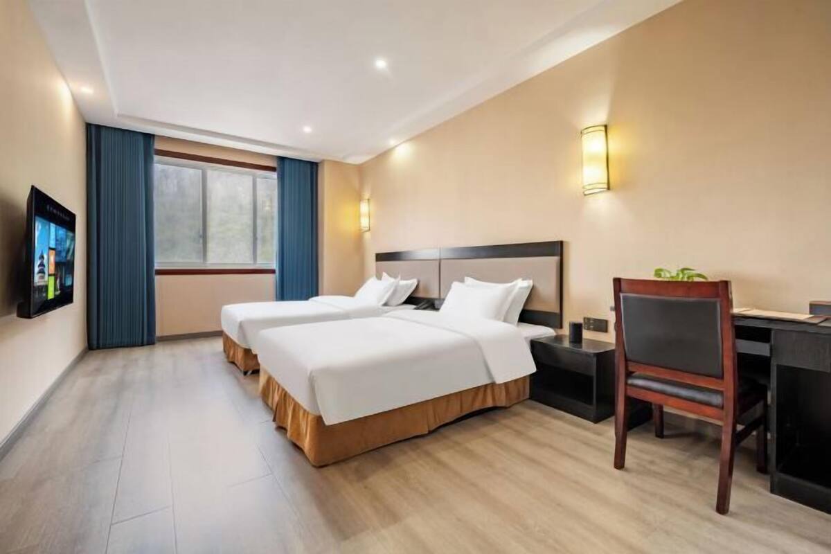 Ein Hotelzimmer mit zwei Betten, einem Schreibtisch, einem Stuhl und einem Fernseher an der Wand.
