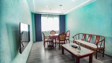 Una habitación con una mesa de comedor de madera, sillas, un sofá, un televisor y un amplio ventanal con cortinas.